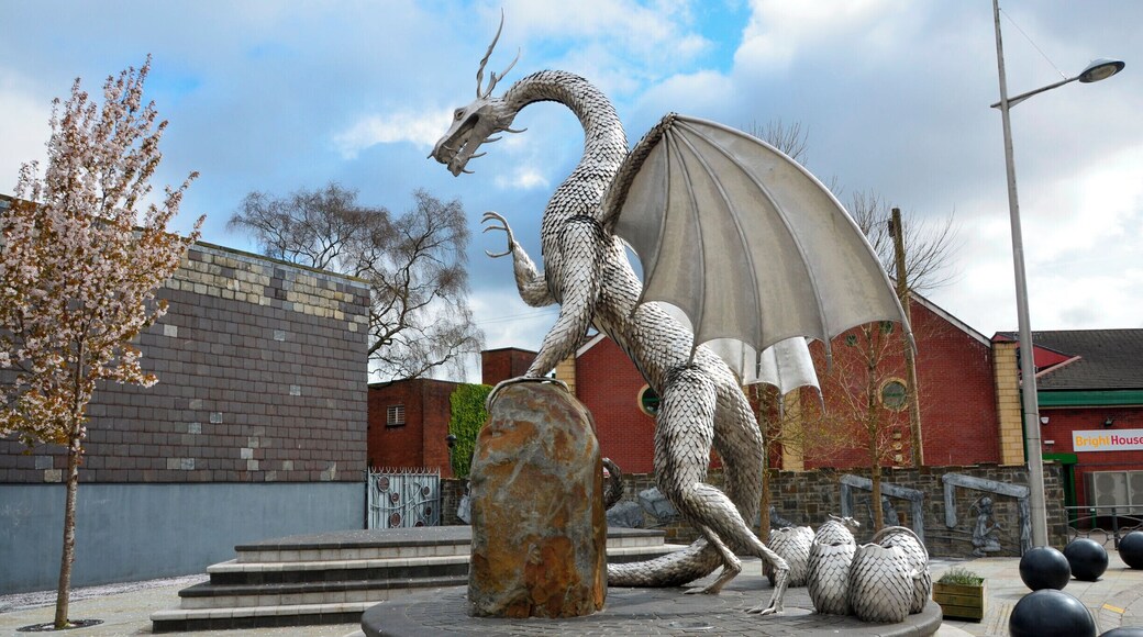 Une sculpture de dragon dans une place publique, avec un bâtiment en briques et un arbre en arrière-plan.