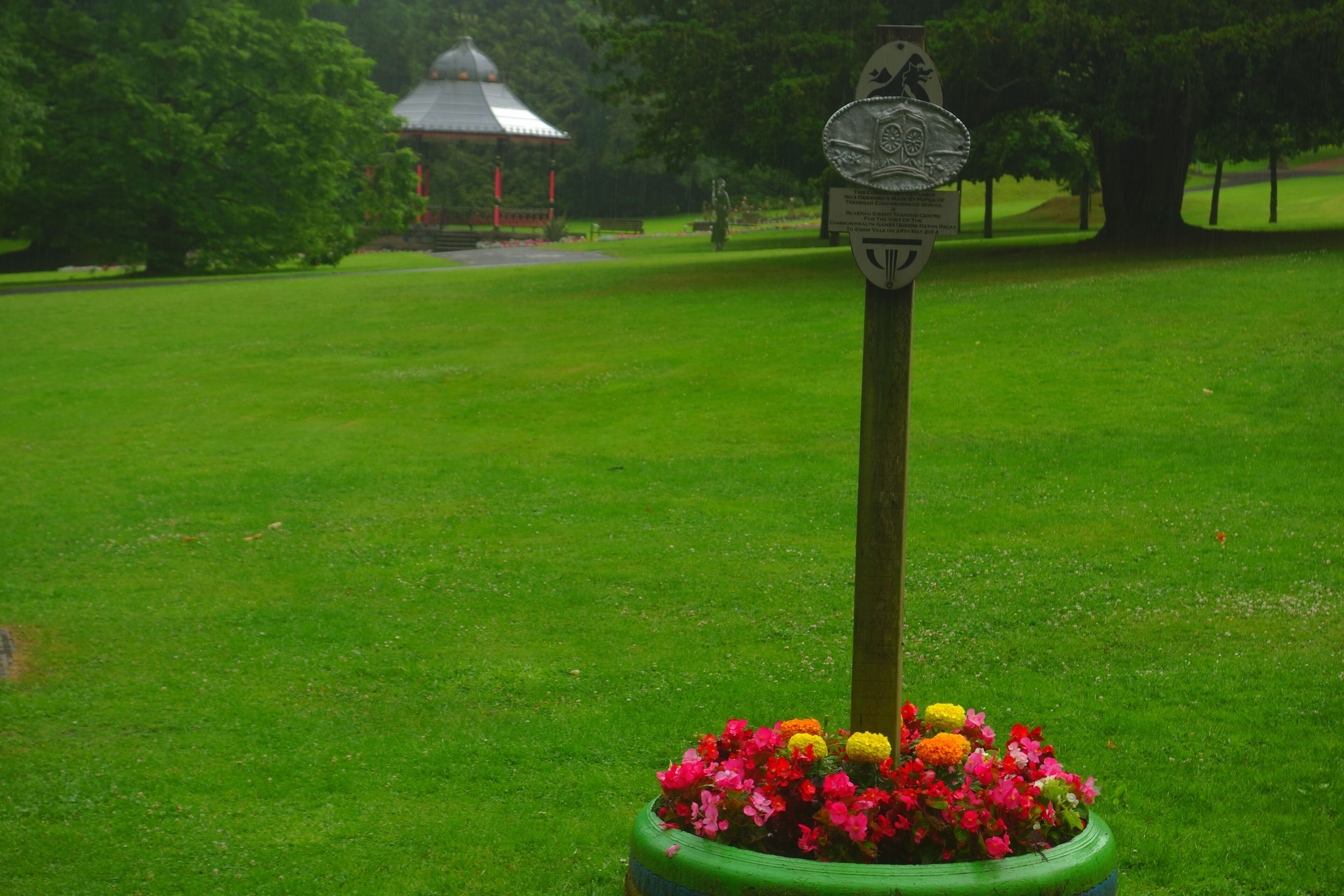 A green lawn with a gazebo in the background and a signpost with a flower pot in the foreground.
