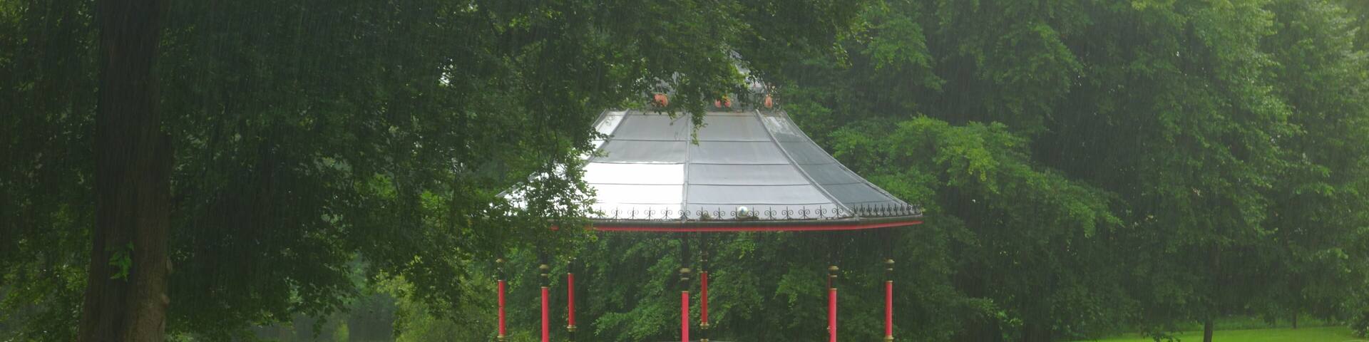A gazebo in a park with a pathway leading to it, surrounded by lush greenery and trees.
