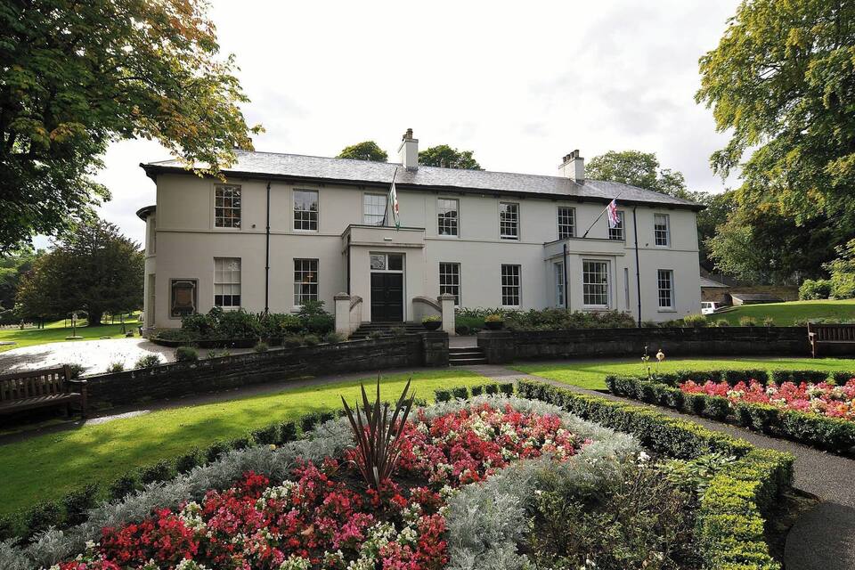 A large white building with a flag, surrounded by well-maintained gardens and trees.