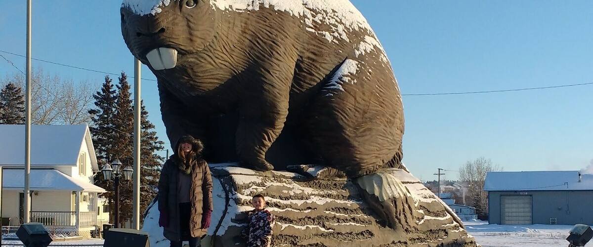 A large bear sculpture in a snowy landscape with footprints leading to it.