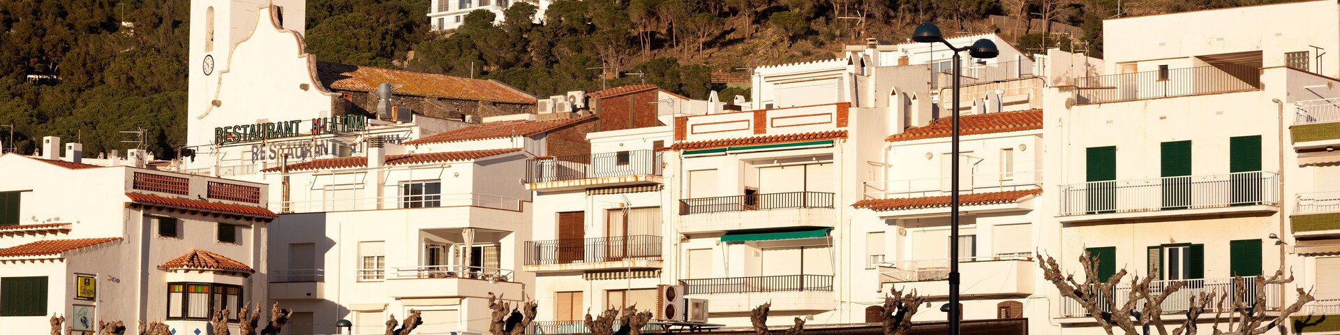 A coastal town with white buildings, a church tower, and parked cars along the street.