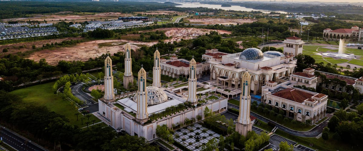 A large mosque with four minarets and a central dome, surrounded by greenery and a river.
