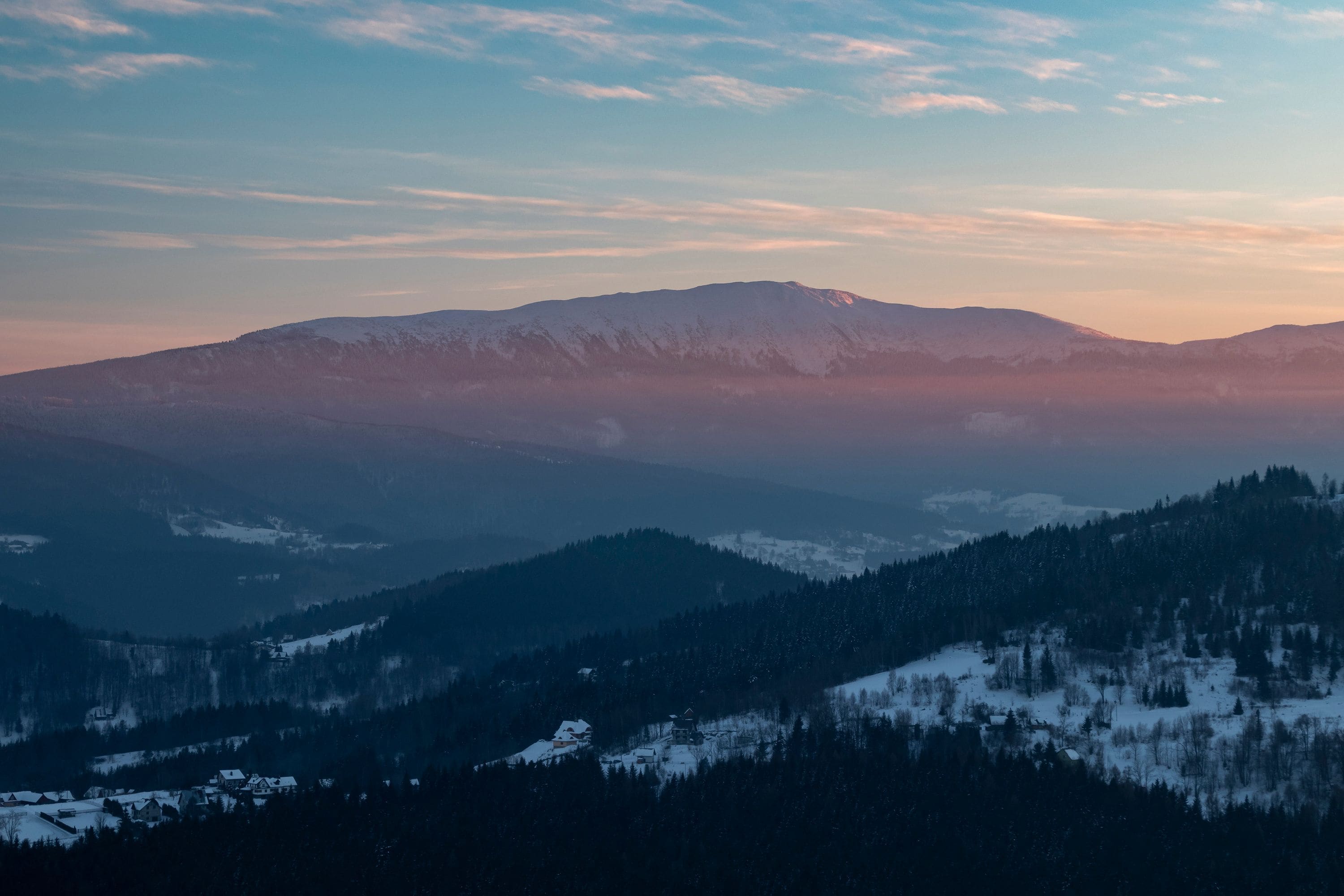 Een bergachtig landschap met besneeuwde toppen en beboste dalen.