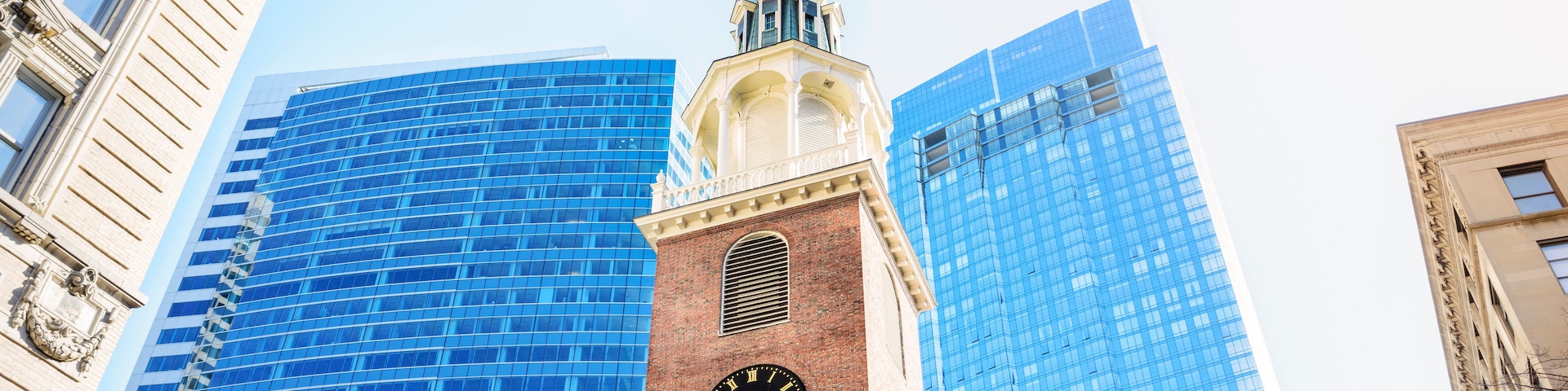 Una torre del reloj con aguja, rodeada de edificios modernos de vidrio.