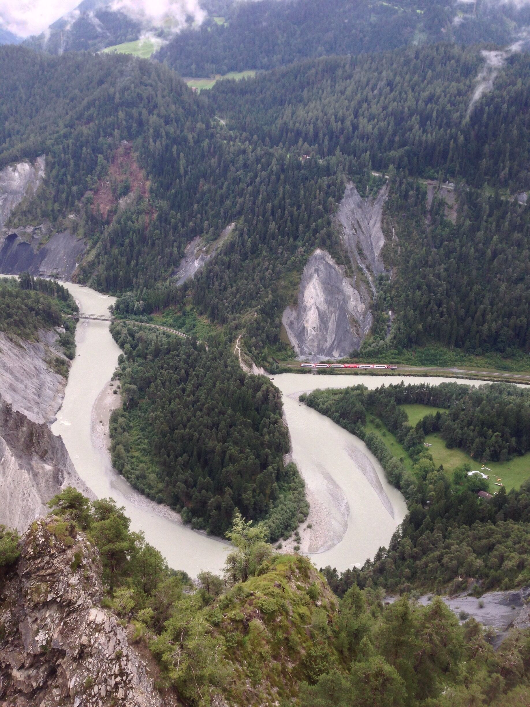A river winding through a mountainous landscape with dense forests and a bridge.