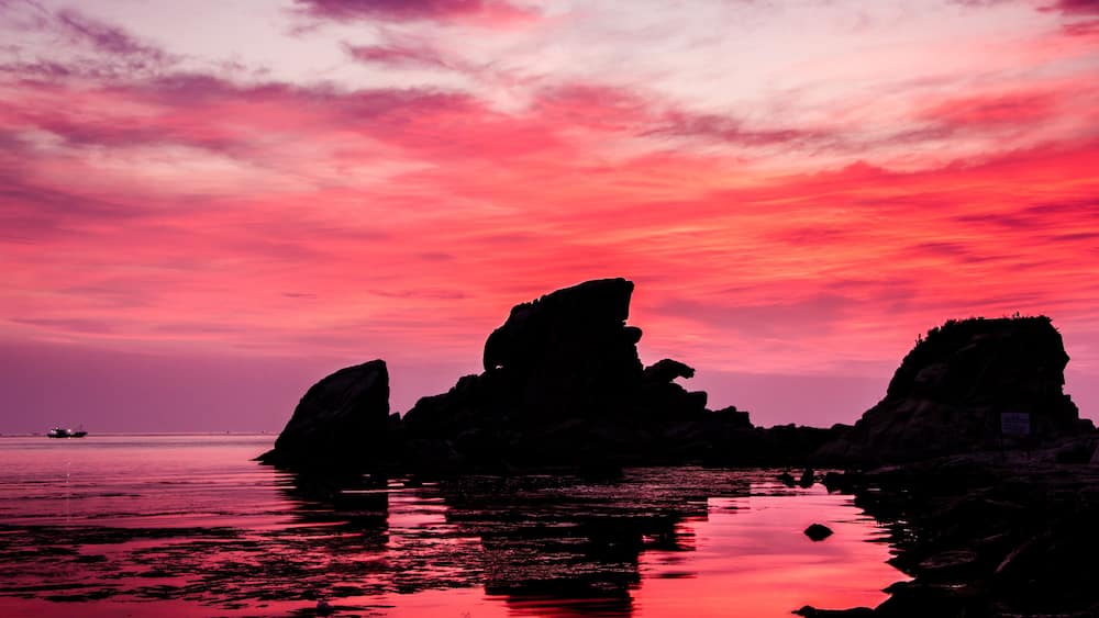 A sunset over a rocky coastline with calm waters reflecting the sky.