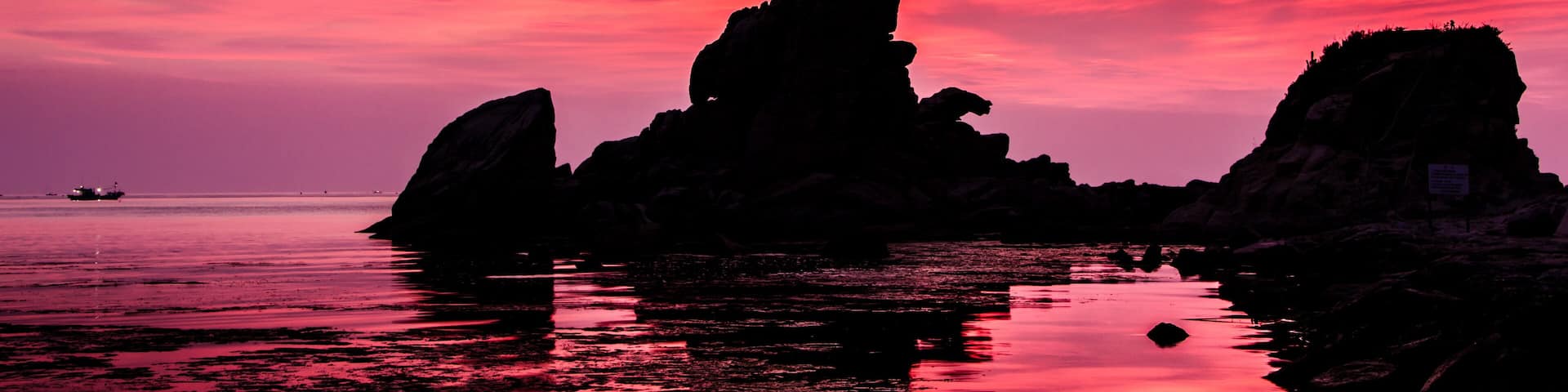 A sunset over a rocky coastline with calm waters reflecting the sky.