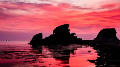 Un atardecer sobre una costa rocosa con aguas tranquilas que reflejan el cielo.