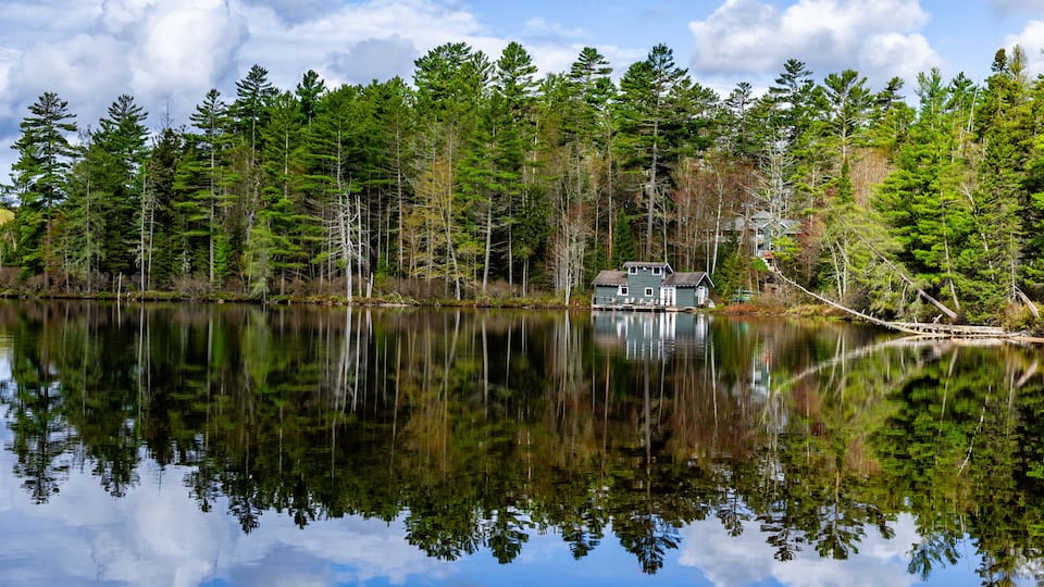 A tranquil lake with dense forest and a small house on the shore.
