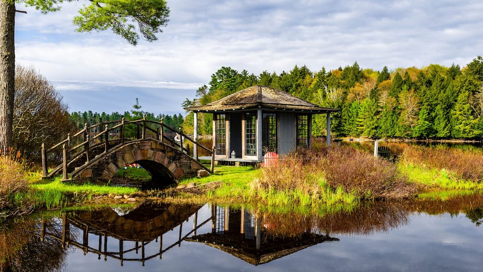 A stone bridge over a calm lake, a small gazebo, and a forested area.