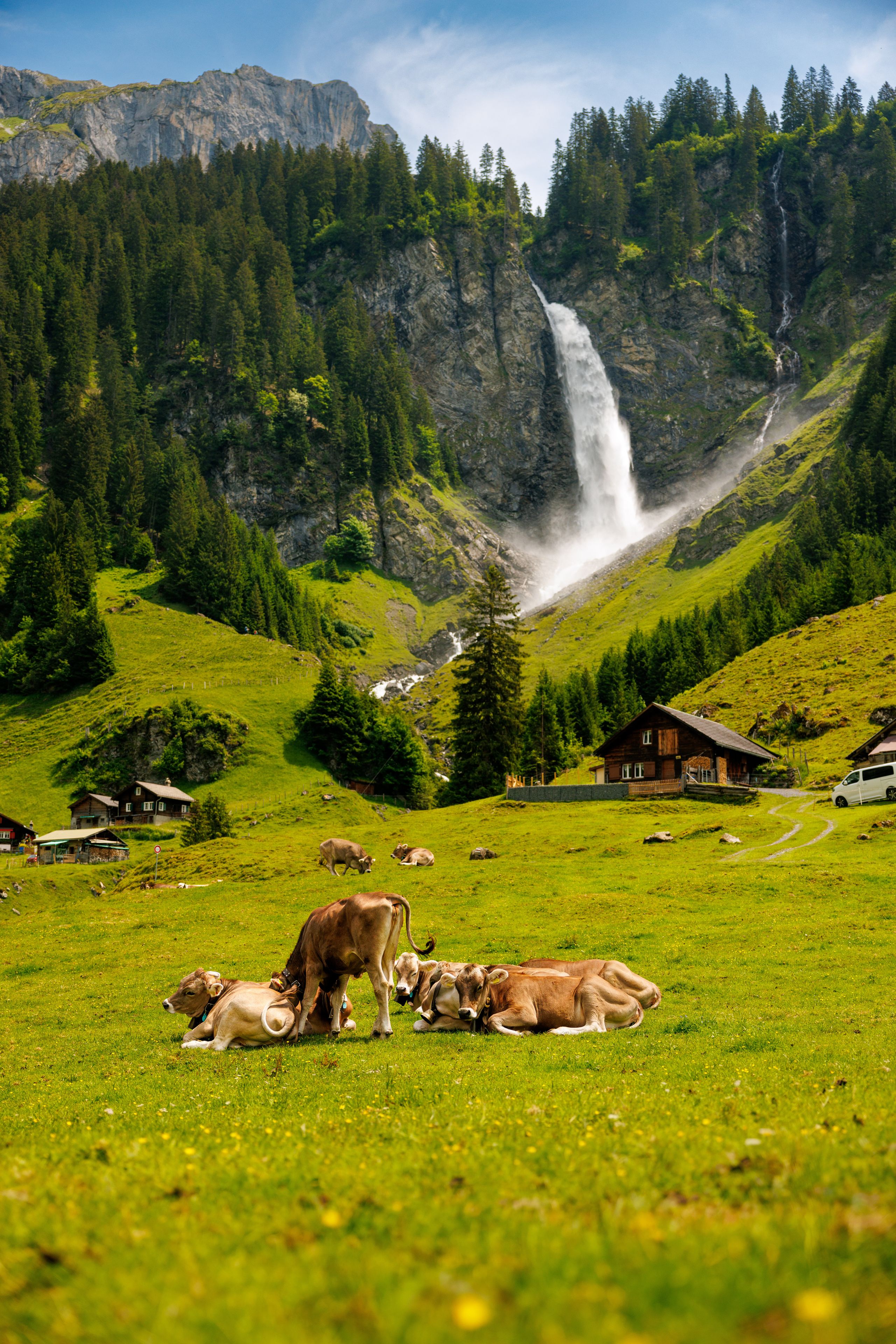 Eine gebirgige Landschaft mit einem Wasserfall, grünen Feldern und Holzhäusern.