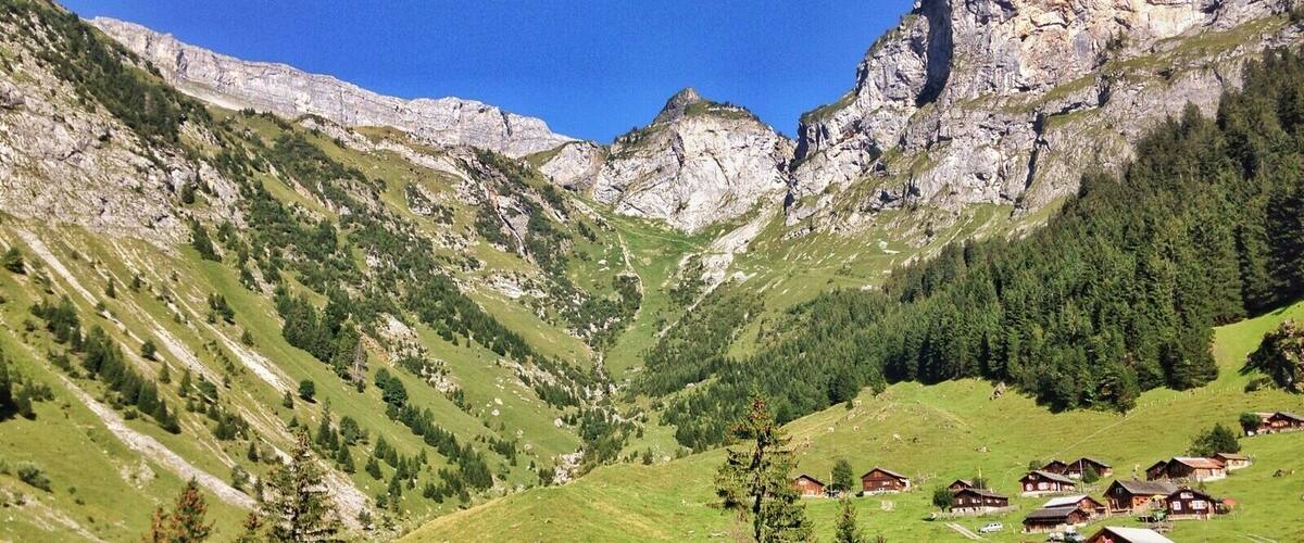 A mountainous landscape with green valleys, rocky cliffs, and a cluster of wooden houses.