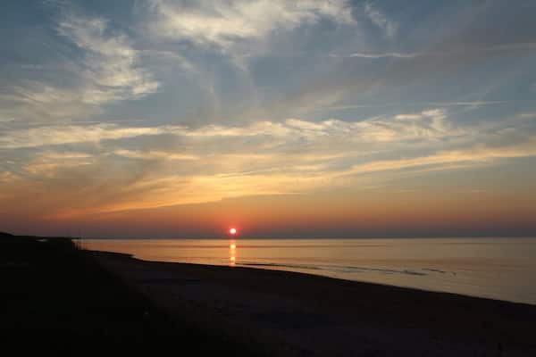 A sunset over a beach with a clear sky and calm sea.