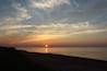 A sunset over a beach with a clear sky and calm sea.