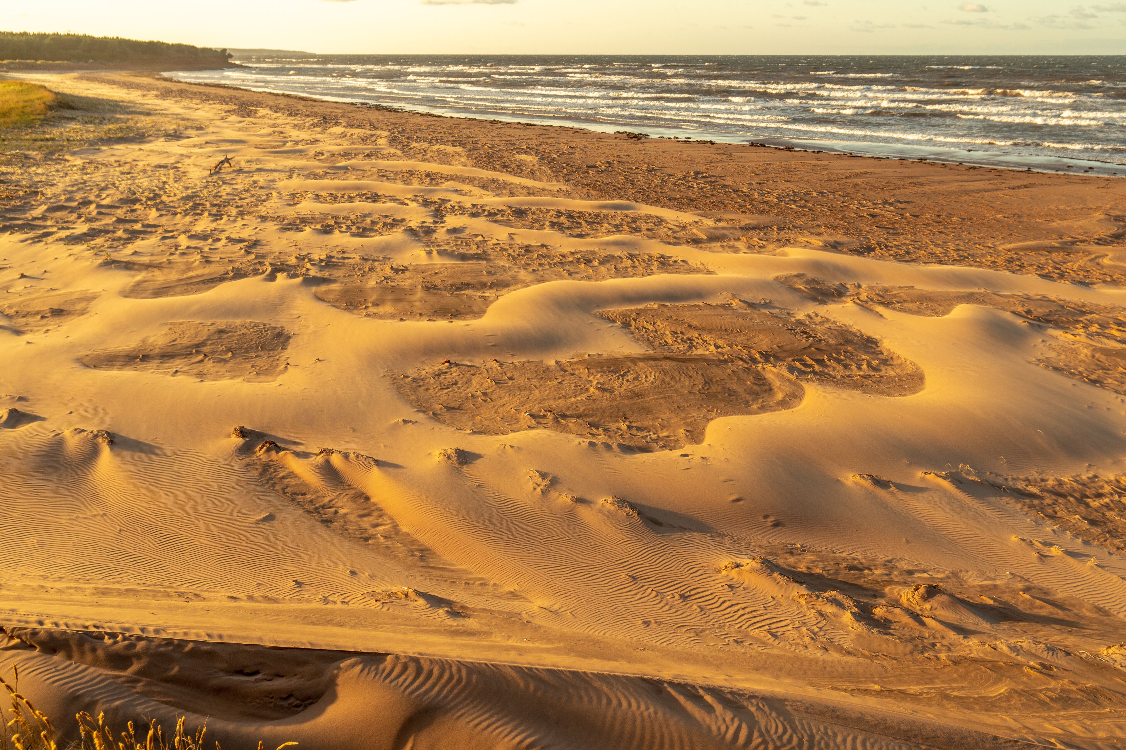The wind formed intricate arrangement of weaved patterns of smooth and rough sand on a beach with waves breaking onto the shore, Brackley Beach, Prince Edward Island, Canada