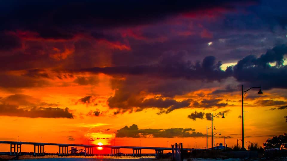 A sunset over a bridge with a city skyline in the background.