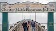 Un muelle llamado Muelle Chester M. McPheerson, Jr., con un letrero de madera que muestra pelícanos y peces, y una placa conmemorativa de su inauguración.