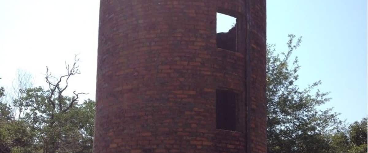 A brick tower with a large hole in the side, surrounded by trees.