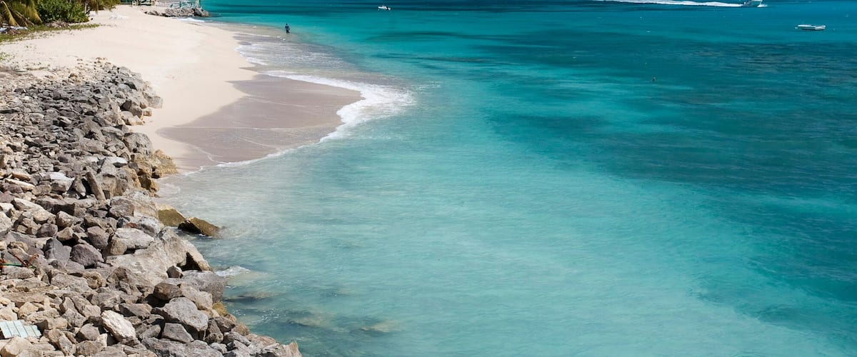 A beach with clear turquoise water, a rocky shoreline, and a distant island.