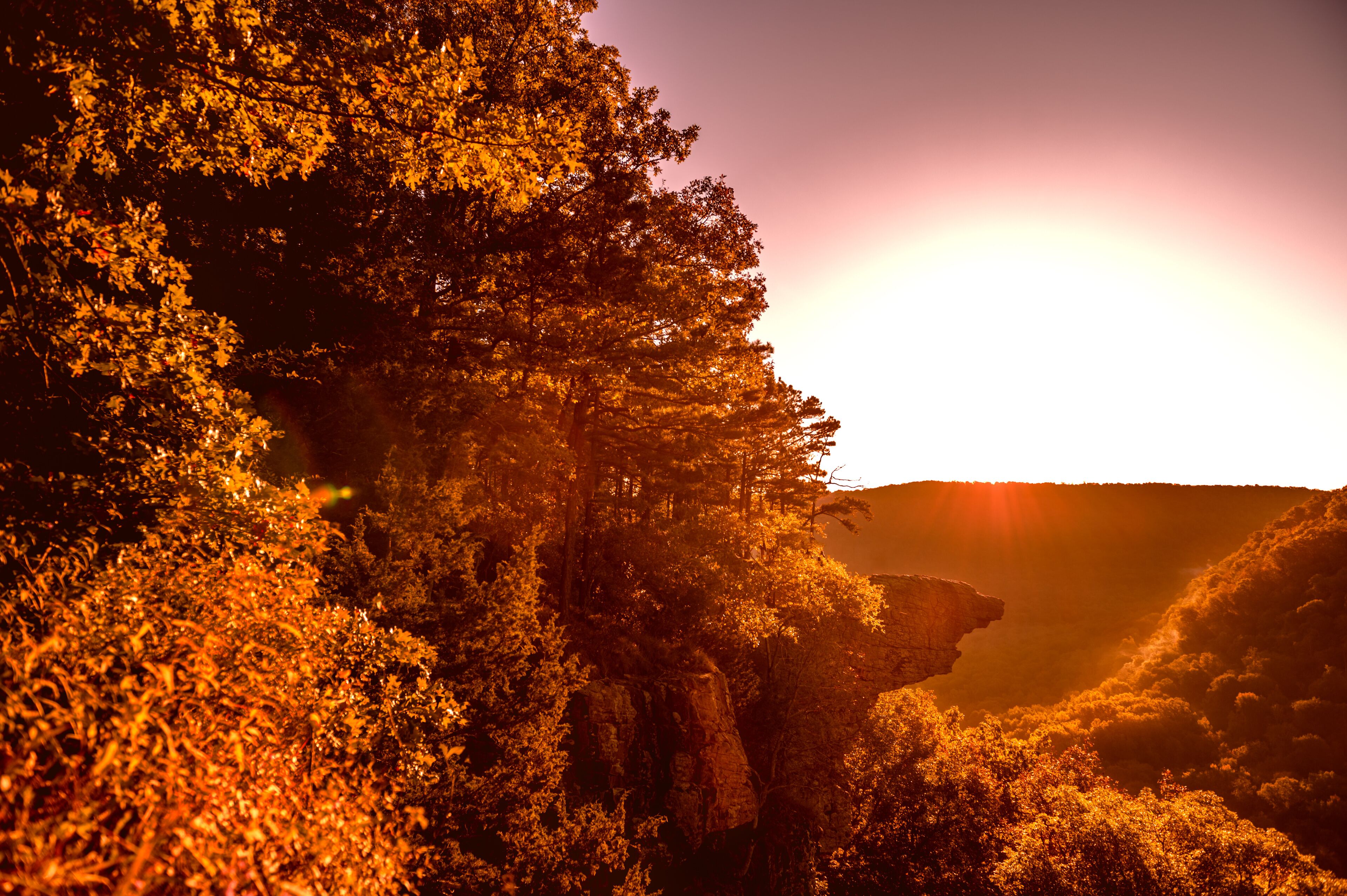 A sunset over a forested valley with a prominent rock formation.