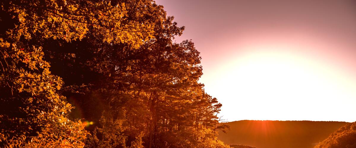 A sunset over a forested valley with a prominent rock formation.