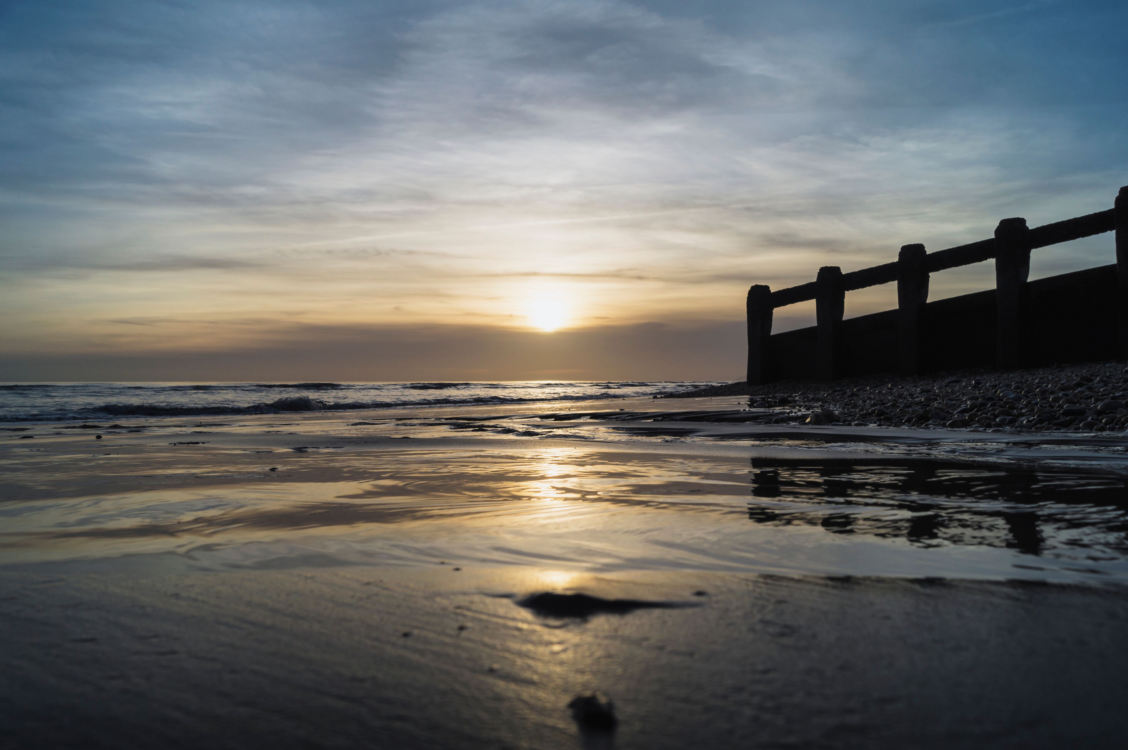 A beach at sunset with a wooden fence in the background.