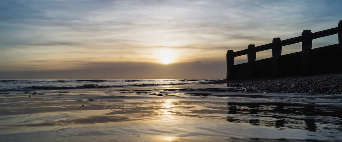 A beach at sunset with a wooden fence in the background.