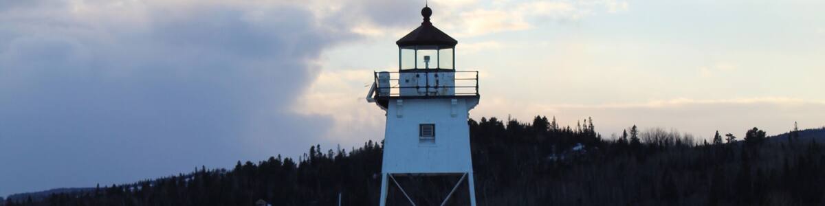 A lighthouse on a snowy pier with a forested hill in the background.