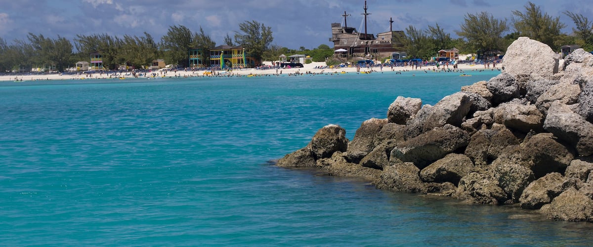 A beach with clear turquoise water, rocky outcrops, and a distant building with a cross.