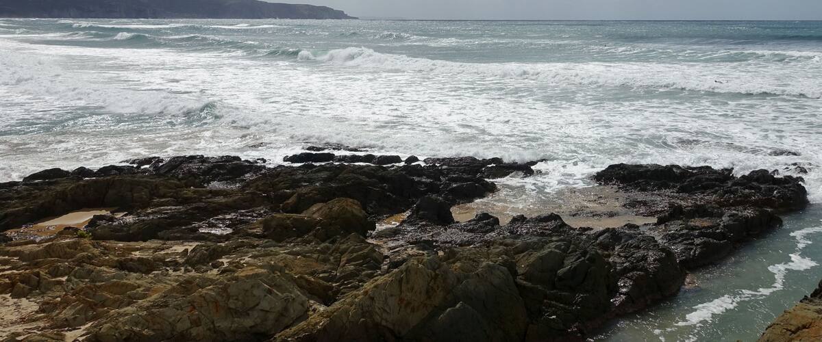 A rocky coastline with waves crashing against the shore and mountains in the background.