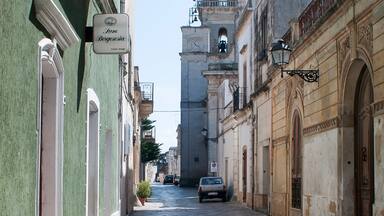 Une ruelle étroite pavée, bordée de bâtiments historiques, avec un clocher et une enseigne indiquant «
La Bodega de la Reina
».