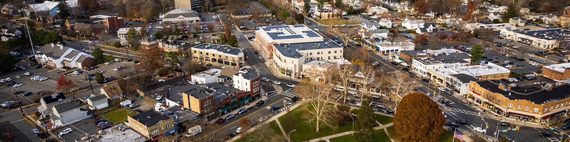 An aerial view of a town with a central roundabout, various buildings, and a large parking lot.