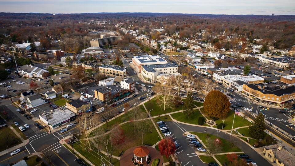 An aerial view of a town with a central roundabout, various buildings, and a large parking lot.