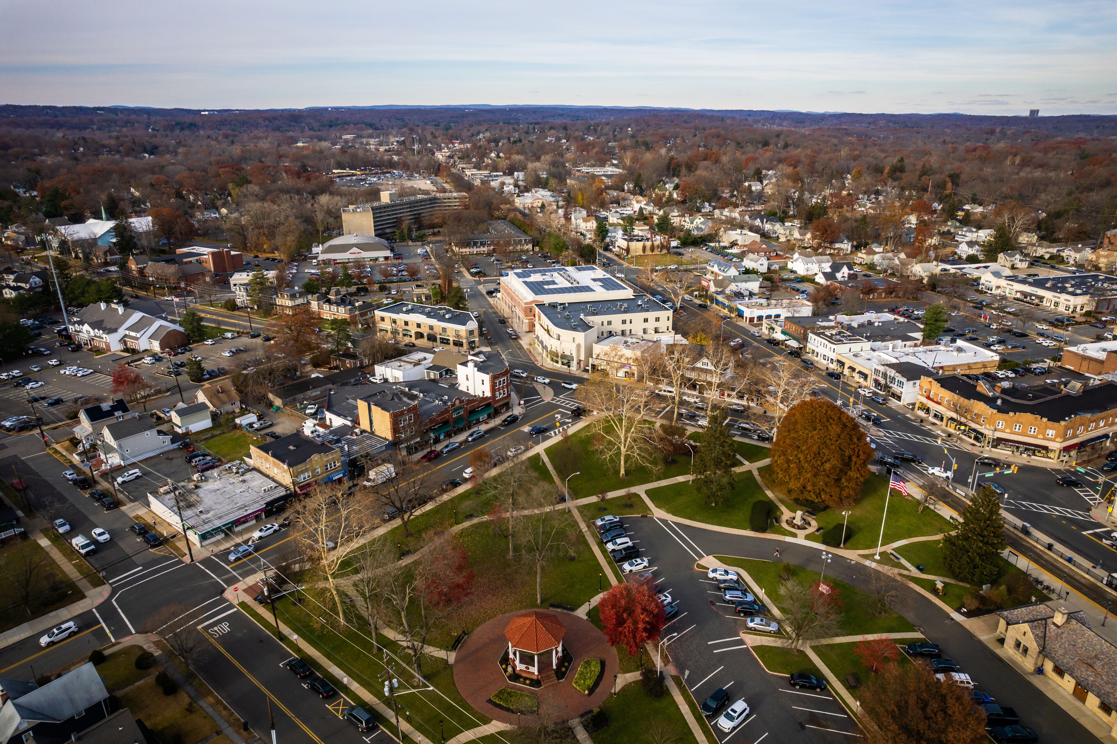 An aerial view of a town with a central roundabout, various buildings, and a large parking lot.