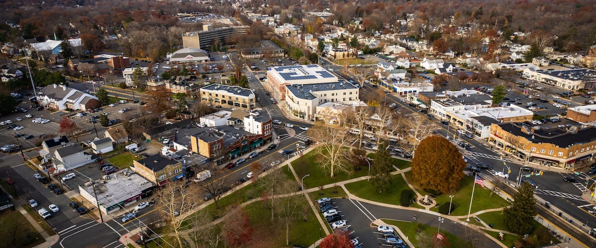 An aerial view of a town with a central roundabout, various buildings, and a large parking lot.