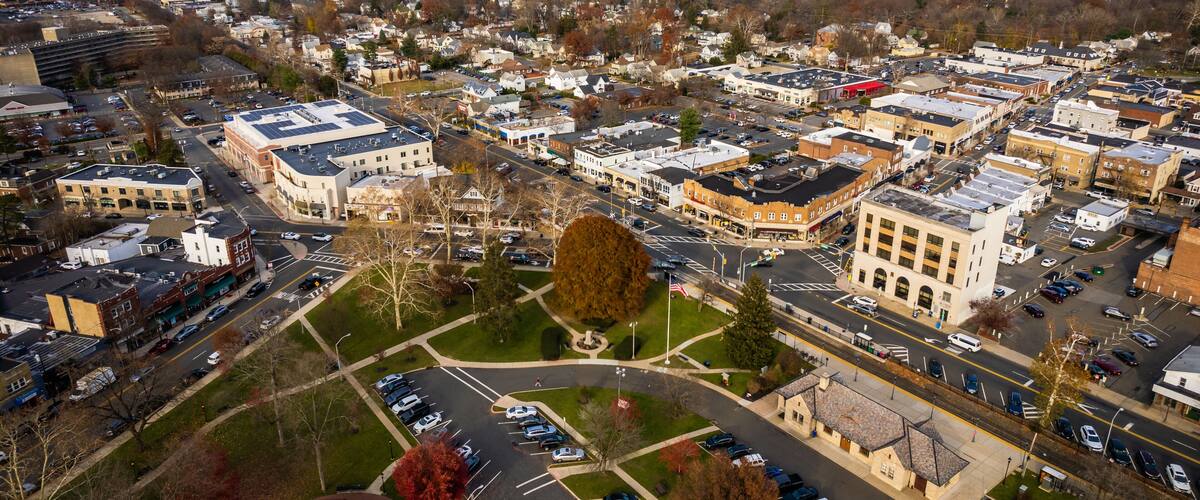 An aerial view of a town with a mix of commercial and residential buildings, a central roundabout, and surrounding green spaces.