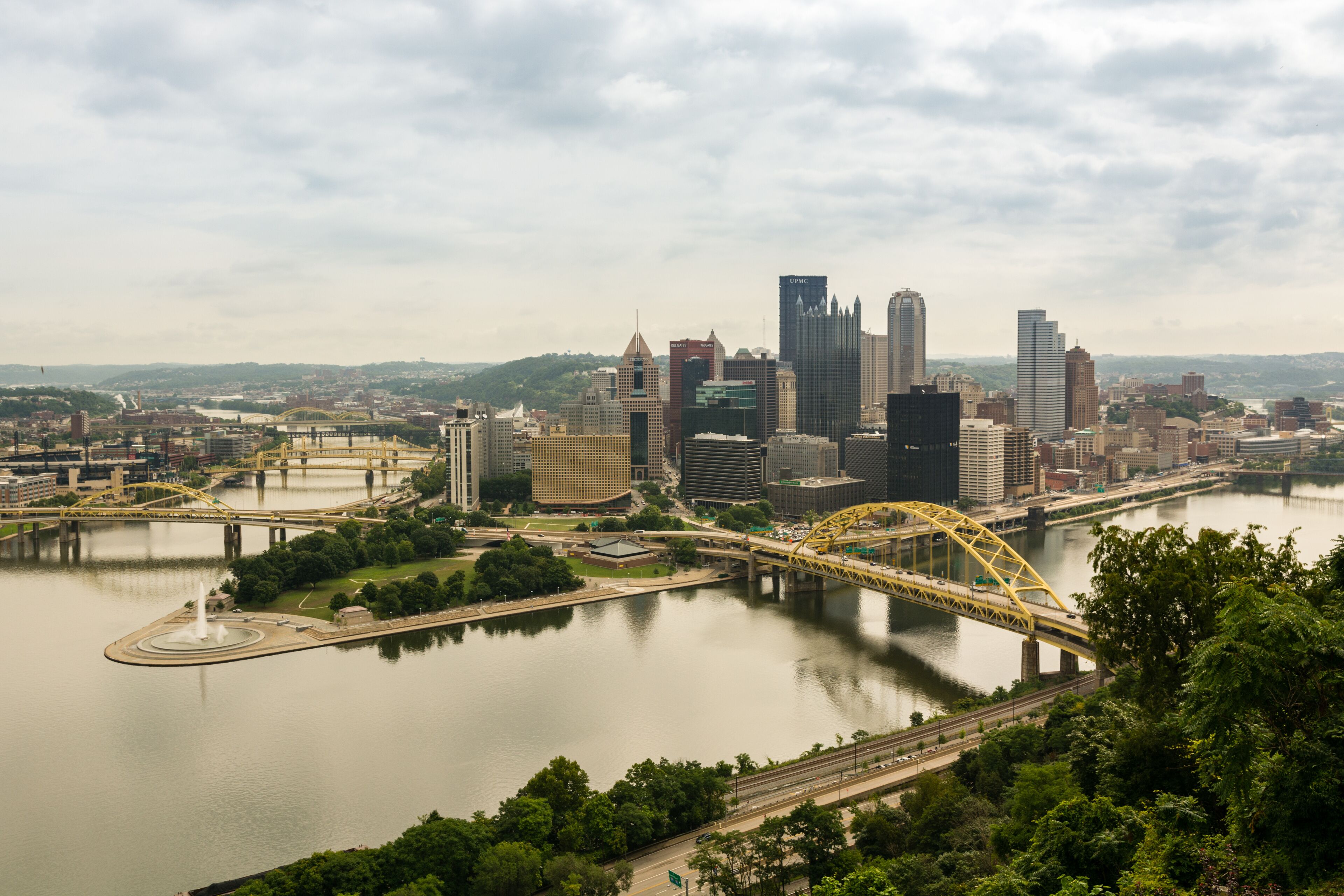A city skyline with modern skyscrapers, a river, and a yellow bridge.
