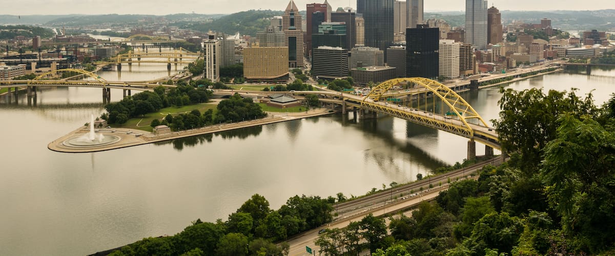 A city skyline with modern skyscrapers, a river, and a yellow bridge.