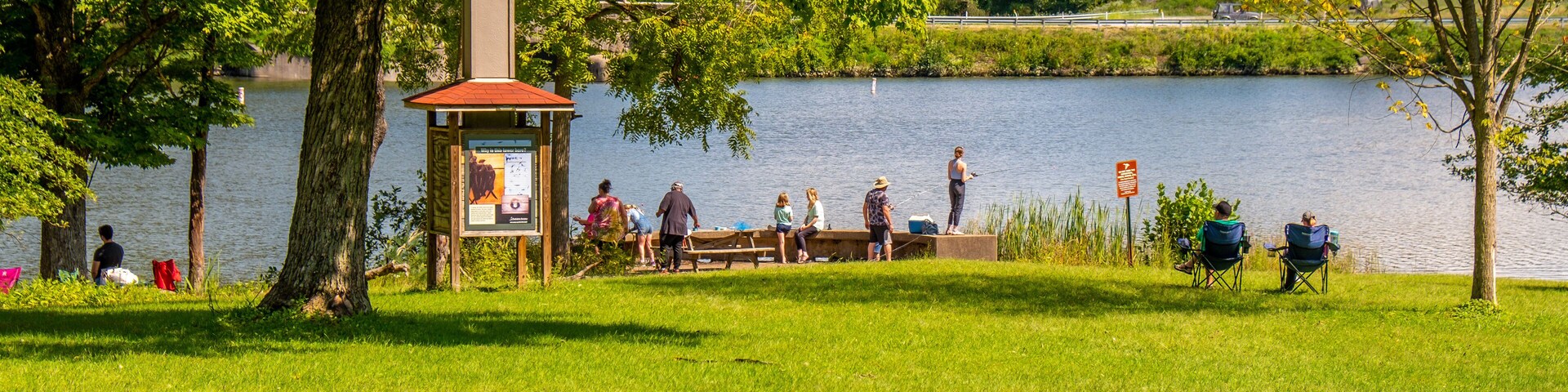 Un parque junto al lago con un pabellón, mesas de picnic y gente relajándose junto al agua.