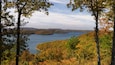 Un lago rodeado de árboles de colores otoñales y colinas al fondo.
