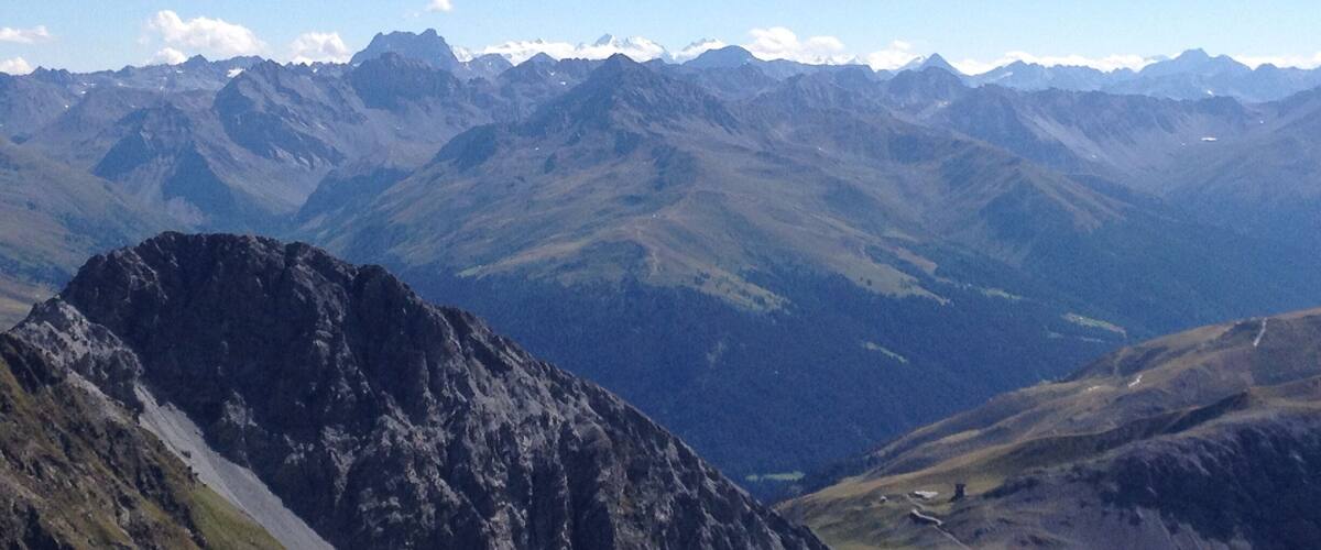 A mountain range with a prominent rocky peak in the foreground and a valley below.