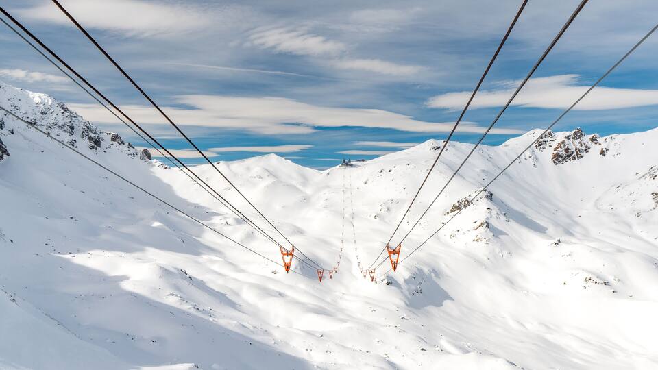 A snowy mountain landscape with ski lift cables and chairlifts.