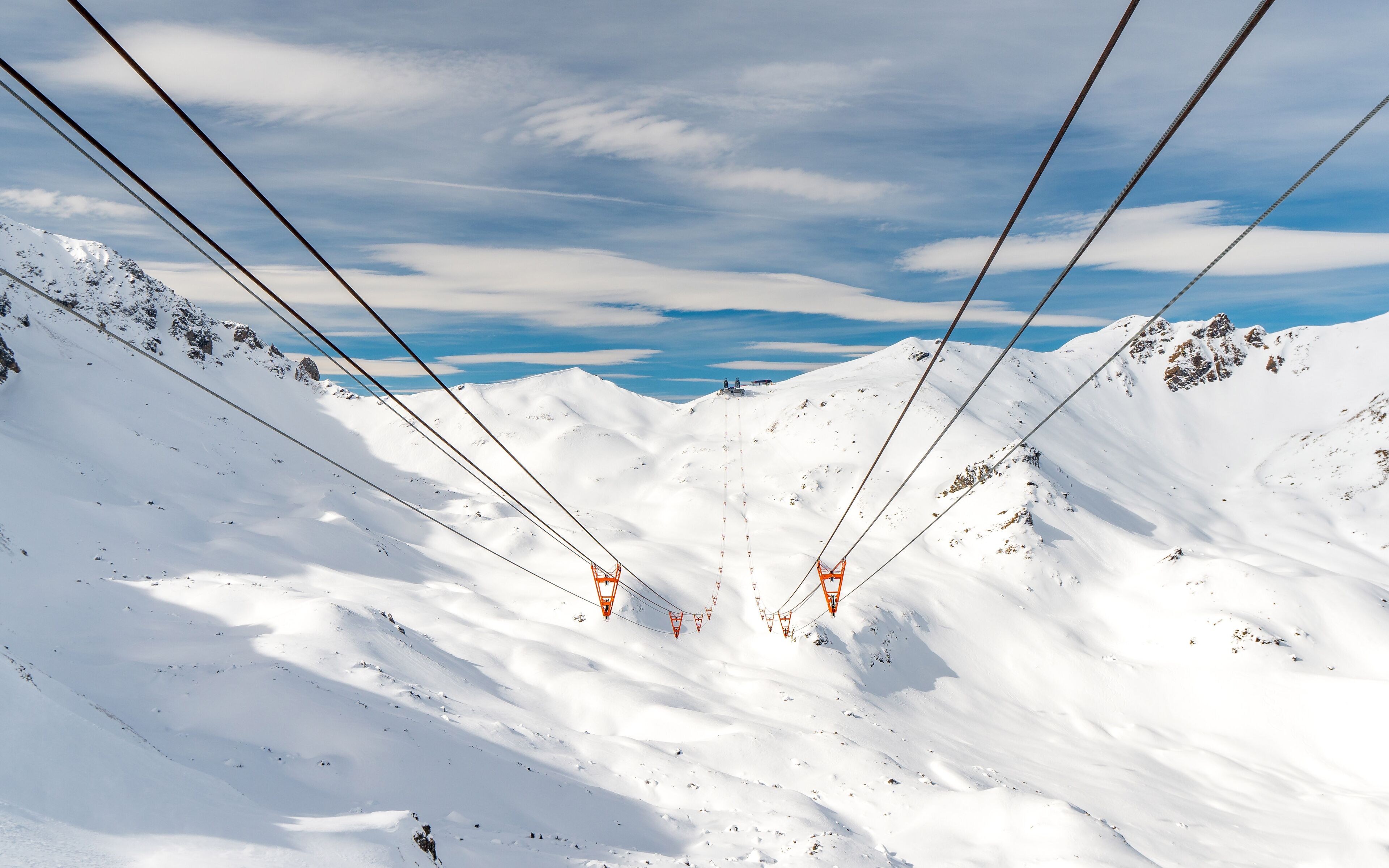 A snowy mountain landscape with ski lift cables and chairlifts.