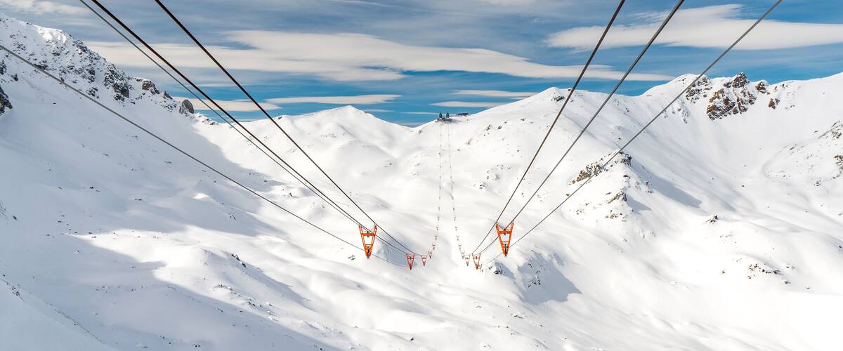 A snowy mountain landscape with ski lift cables and chairlifts.
