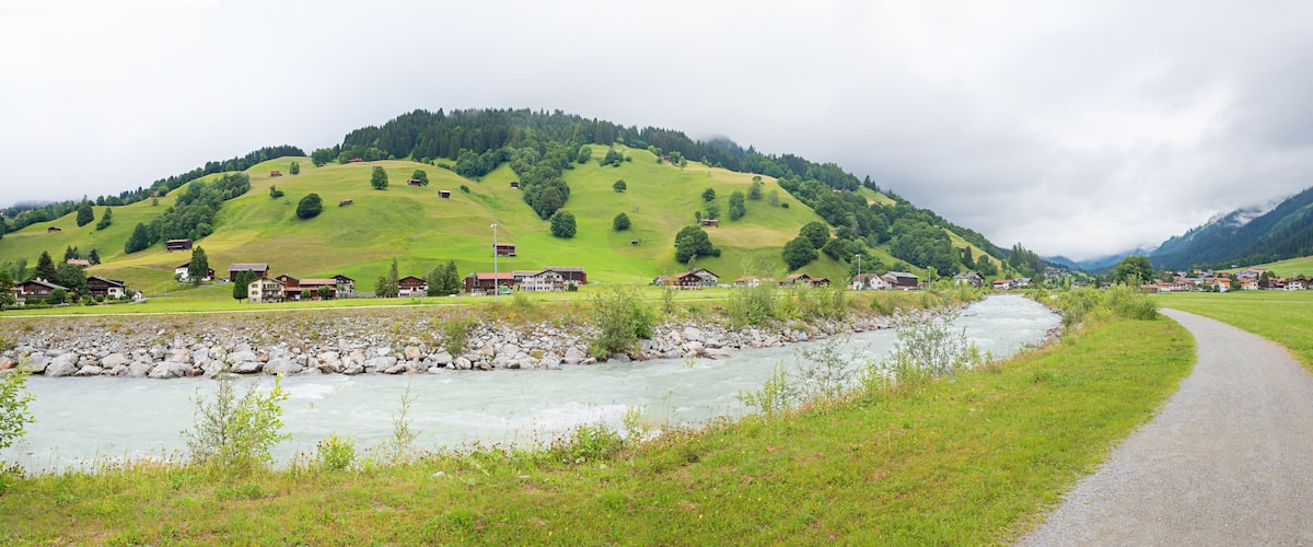 A river flowing through a valley with houses on the hillside and a path alongside the river.