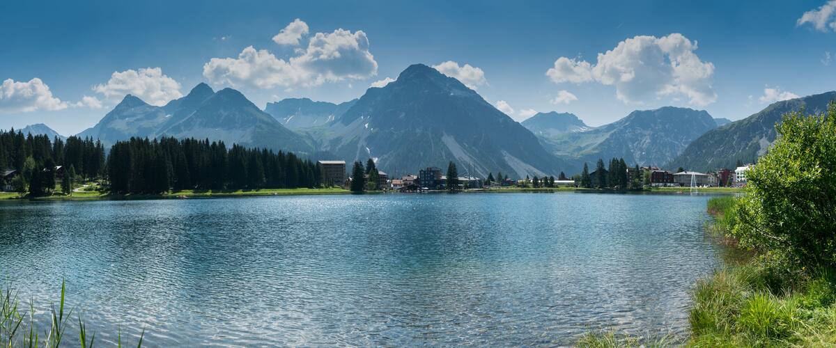 A lake surrounded by mountains, with buildings and trees along the shore.