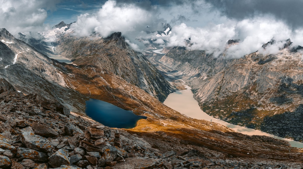 A mountain landscape with a lake, rocky terrain, and snow-capped peaks.