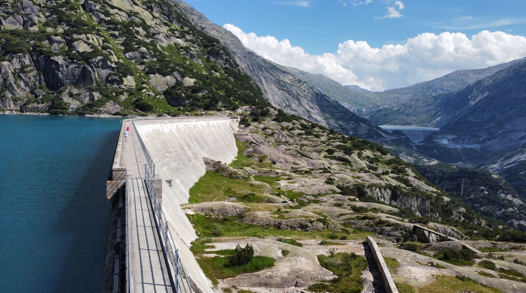 A dam with a person walking on the walkway, surrounded by rocky terrain and a lake.