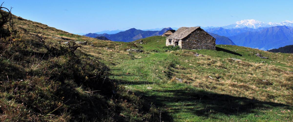 A stone house on a grassy hillside with a clear blue sky and snow-capped mountains in the background.